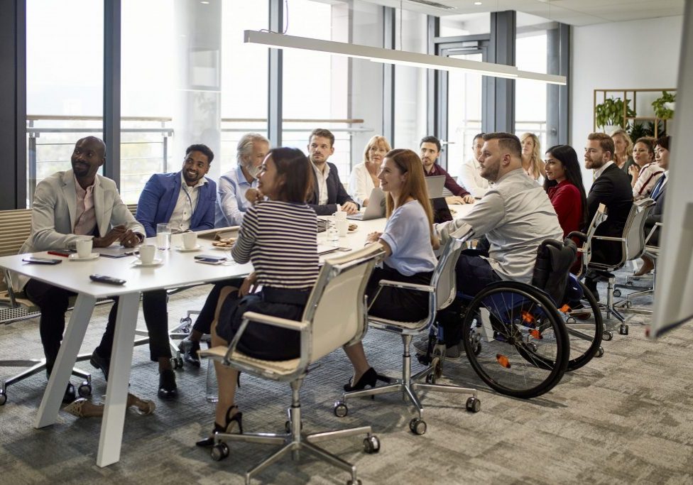 Comprehensive viewpoint of diverse group of business executives sitting together at conference table and looking at camera.